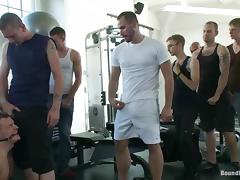A tied up guy sucks huge dicks and get toyed in a gym